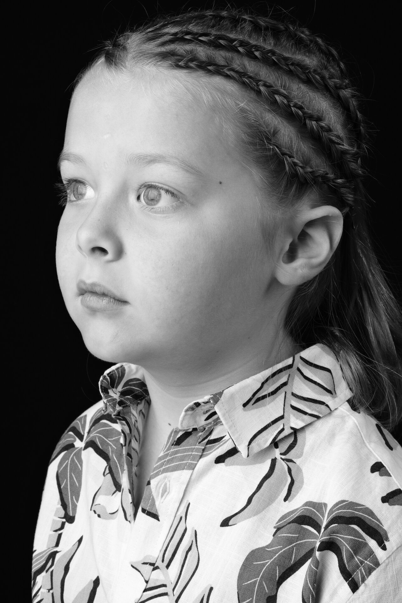 George Rouse black and white profile headshot with braided hair and leaf-patterned shirt against dark background
