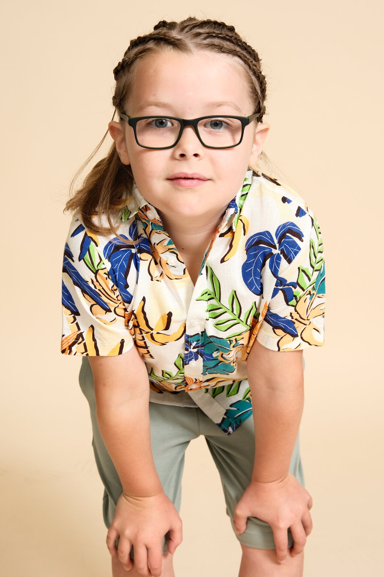 George Rouse three-quarter shot wearing glasses and tropical print shirt, leaning forward with hands on knees against cream background